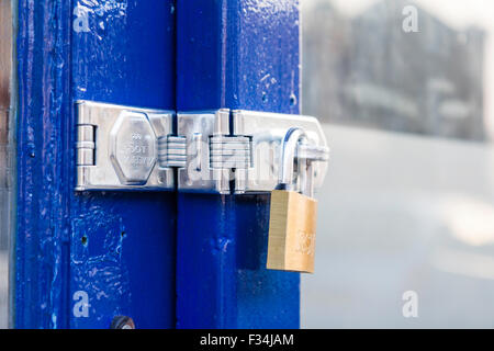 Golden colour padlock on silver lock on blue painted door frame. Close up of locked padlock. Stock Photo