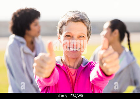Sporty woman doing thumbs up in front of friends Stock Photo