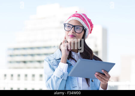 Thoughtful woman holding tablet pc with finger on cheek Stock Photo