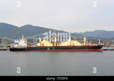 Large piles of yellow sulphur are ready to be loaded into the holds of this tanker in Vancouver, Canada Stock Photo