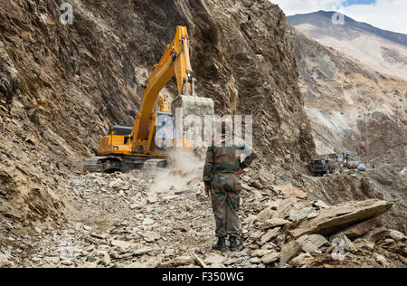 Officers from Border Roads Organization and GREF watch as excavator clears hazardous Himalayan mountain road following landslide Stock Photo