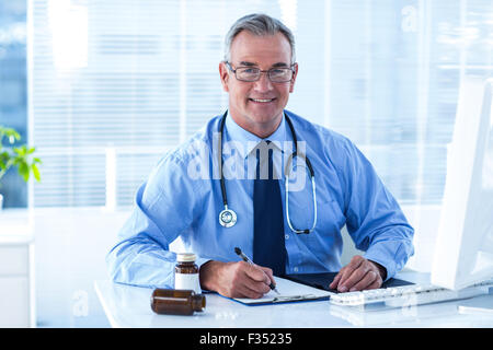 Portrait of smiling male doctor writing on document in clinic Stock Photo
