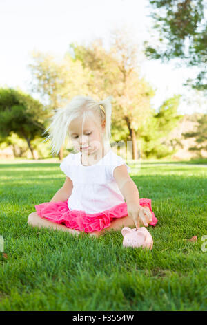 Cute Little Girl Having Fun with Her Piggy Bank Outside on the Grass. Stock Photo