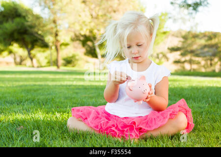 Cute Little Girl Having Fun with Her Piggy Bank Outside on the Grass. Stock Photo