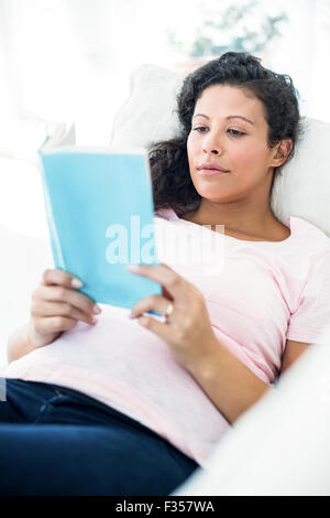 Pregnant woman reading book on sofa Stock Photo