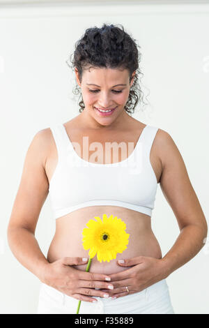 Happy pregnant woman touching her stomach while holding yellow flower Stock Photo