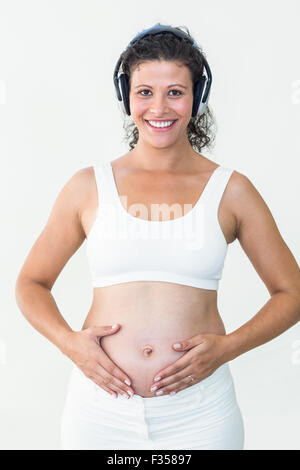 Smiling pregnant woman listening to music while touching her belly Stock Photo