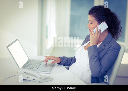 Pregnant businesswoman talking on mobile phone while working Stock Photo