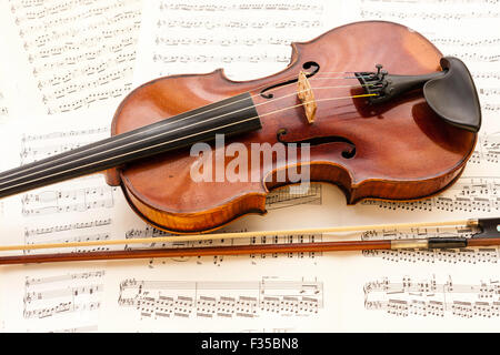 A restored violin marked Thouvenel, Paris, from circa 1800, with a vuillaume bow next to it, resting on a background of sheet music. Stock Photo