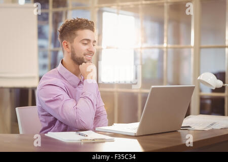 Businessman with hand on chin working with laptop Stock Photo