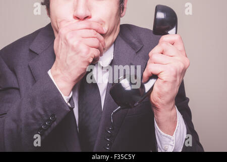 A young businessman is on the phone and covering his mouth in shock Stock Photo