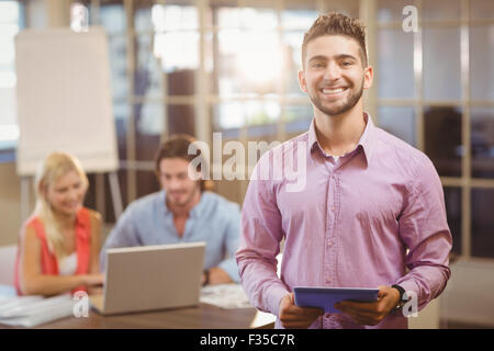 Businessman using digital tablet in office with colleagues on laptop Stock Photo