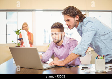 Businessmen working on laptop with female colleague in background Stock Photo