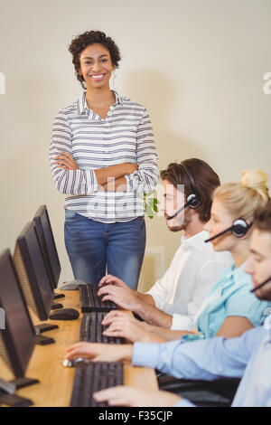 Smiling businesswoman with arms crossed standing at employees Stock Photo