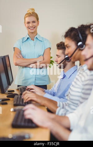 Happy businesswoman with arms crossed standing at employees Stock Photo