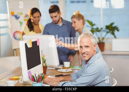 Confident businessman using on computer with colleagues in background Stock Photo