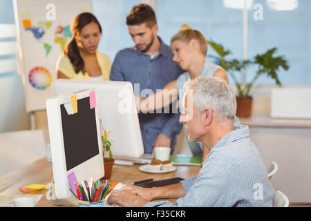 Businessman using on computer with colleagues in background Stock Photo