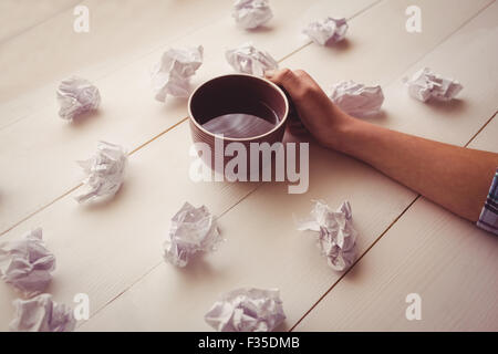 Hands holding coffee cup next to paper balls Stock Photo