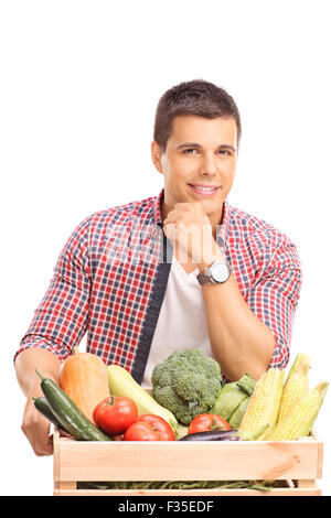 Young man leaning on a wooden crate full of fresh vegetables and looking at the camera isolated on white background Stock Photo