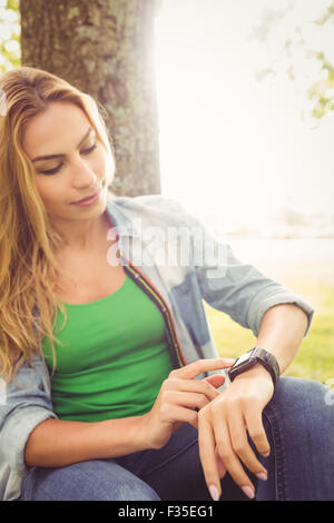 Woman touching smart watch while sitting under tree Stock Photo