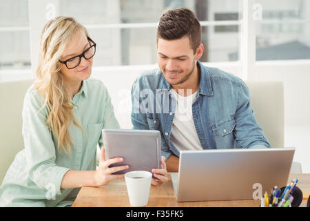 Smiling woman wearing eyeglasses showing digital tablet to man Stock Photo
