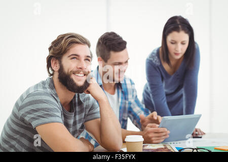 Smiling man looking away with coworkers using digital tablet Stock Photo