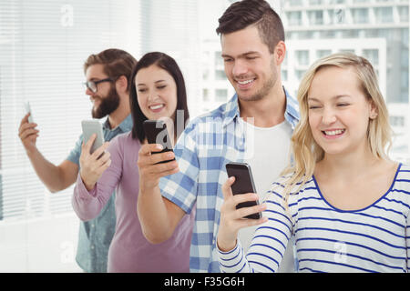Smiling business people using smartphones while standing in row Stock Photo