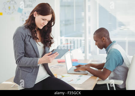 Woman using digital tablet while sitting on desk with man working Stock Photo