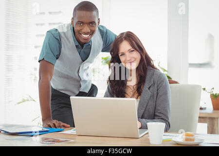 Portrait of smiling businesswoman working on laptop with coworker at desk Stock Photo