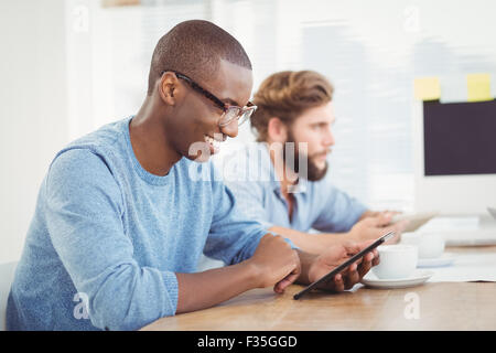 Happy man wearing eyeglasses while using digital tablet at desk Stock Photo