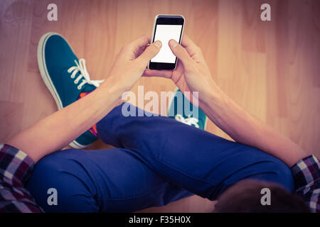 Hipster using smartphone while sitting on hardwood floor Stock Photo