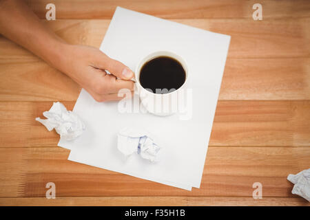 Man holding black coffee cup on paper at desk Stock Photo