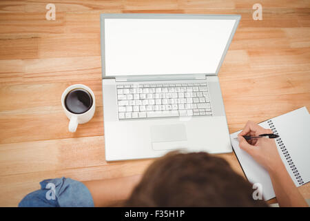 Hipster writing on spiral notebook by laptop at desk in office Stock Photo