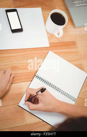 Man writing on spiral notebook at desk in office Stock Photo