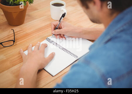 Hipster writing on spiral book at desk Stock Photo