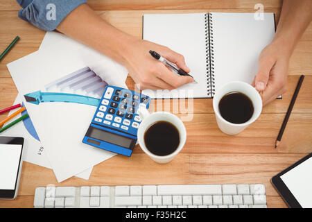 Hipster holding coffee while writing on spiral notebook Stock Photo