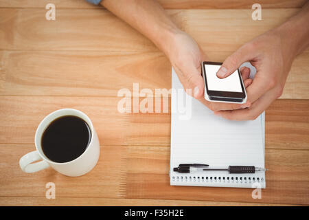 Hipster using smartphone with coffee and notepad on table in office Stock Photo