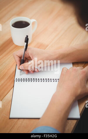Hipster writing on spiral notebook at desk in office Stock Photo