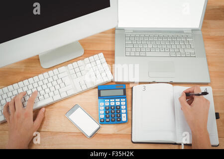 Businessman writing on diary using computer at desk Stock Photo