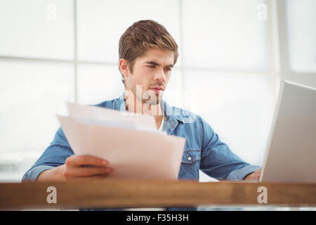 Hipster holding documents while working on laptop in office Stock Photo