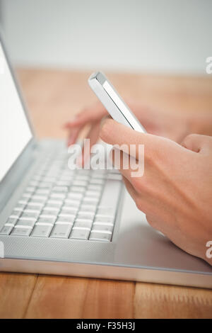 Man using mobile phone while typing on laptop Stock Photo
