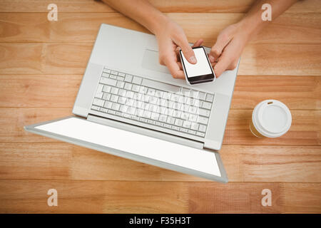 Man using smartphone while laptop and disposable cup on desk Stock Photo