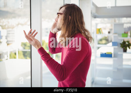 Hipster talking on cellphone standing by window Stock Photo