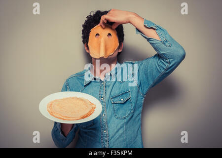 Young man has cut eyeholes in a pancake and is wearing it on his face Stock Photo