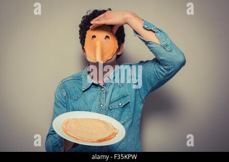 Young man has cut eyeholes in a pancake and is wearing it on his face Stock Photo