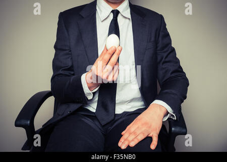 A young businessman sitting in an office chair is holding a boiled egg Stock Photo
