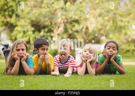 Happy classmates grimacing and lying in grass Stock Photo