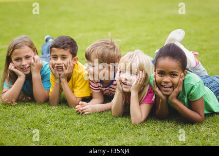 Smiling classmates lying in a row in grass Stock Photo