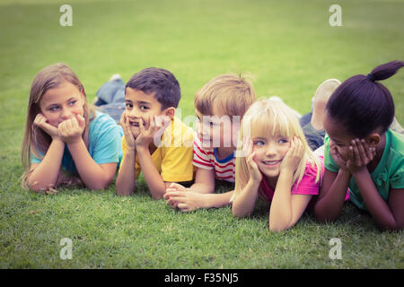 Smiling classmates lying in a row in grass Stock Photo