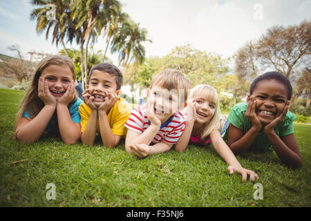 Smiling classmates lying in a row in grass Stock Photo